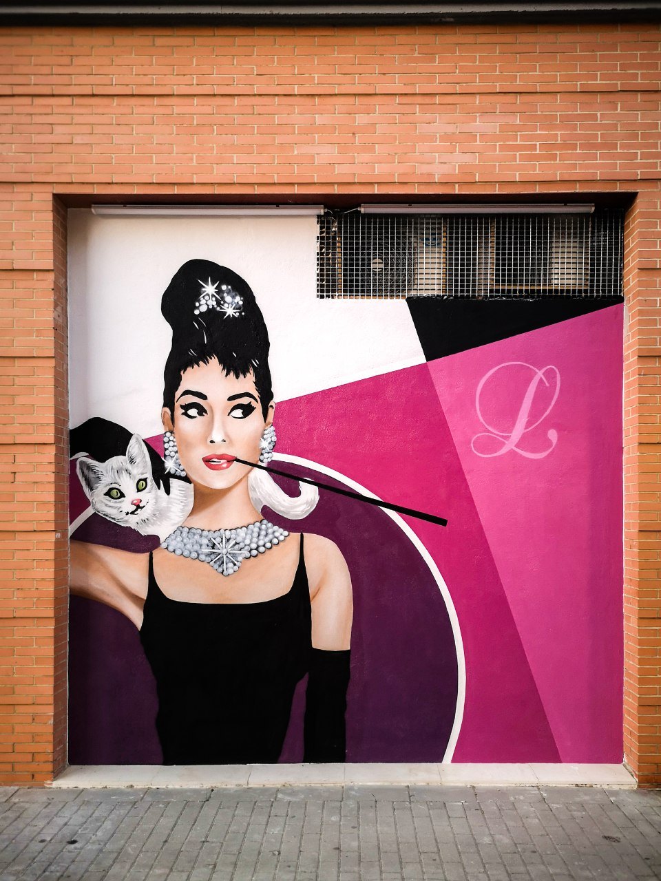 Mural de la fachada: mujer con moño alto, collar y boquilla, con un gato blanco y una L sobre fondo magenta