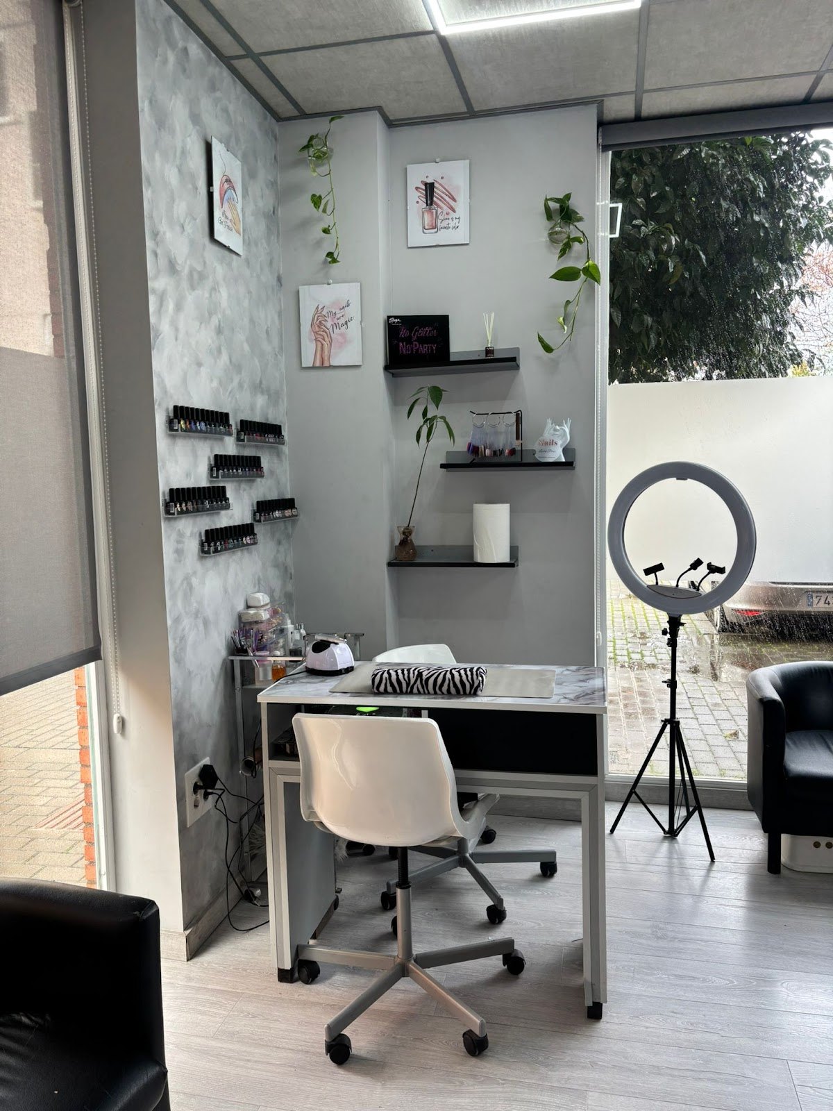 Rincón de manicura junto al escaparate, con mesa blanca, aro de luz y esmaltes en la pared