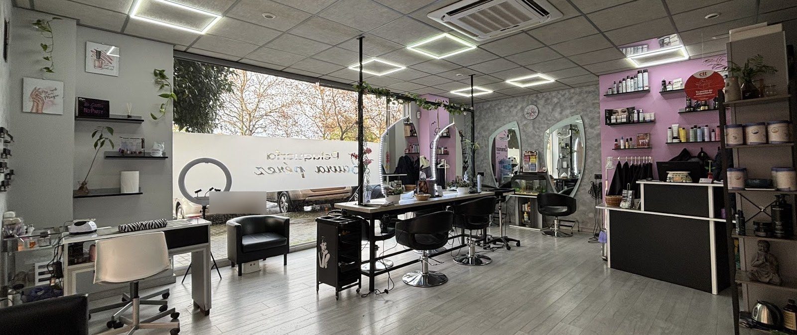 Salón con tocadores, espejos ovalados, mesa de manicura y estanterías de productos sobre pared lila